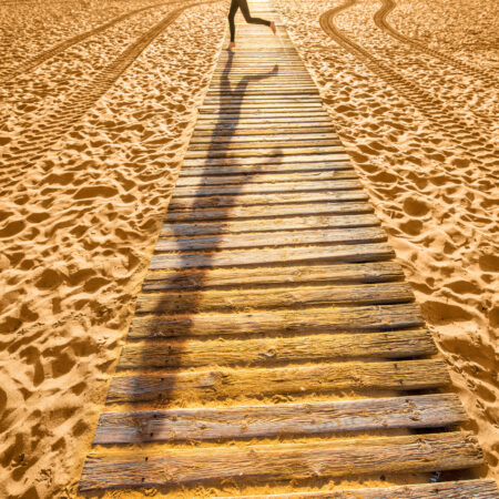 View on sandy beach with wooden footpath and shadow of running woman